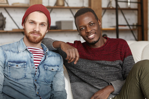 Interracial friendship concept happy african american male casual sweater resting elbow his best friend s shoulder while sitting white couch coffee shop talking having fun together